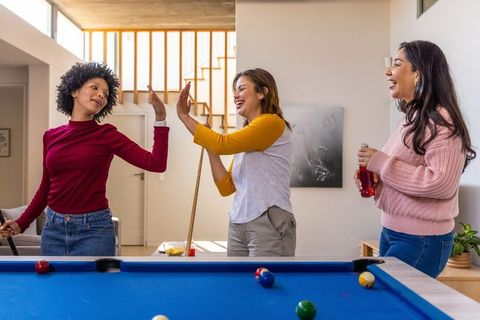 Diverse friends high-fiving while playing pool at home, indoor recreation and laughter