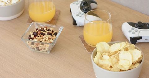 Cozy game night snack spread with potato chips, trail mix, orange juice and controllers