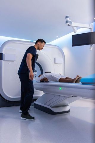 Asian technician assisting african american patient during mri scan in radiology suite