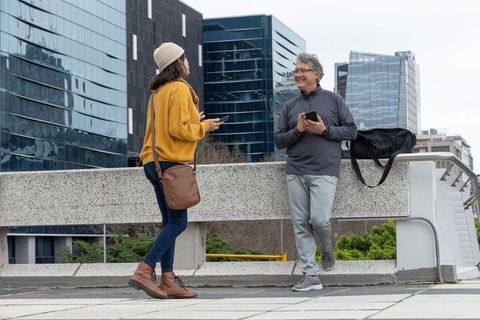 Senior man and woman chatting on urban plaza, casual conversation while holding phones