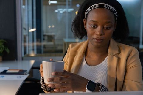 African american professional woman holding mug while working on laptop in office late