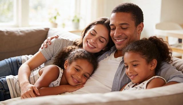 Loving family cuddling on sofa, parents and kids smiling and relaxing in bright living room