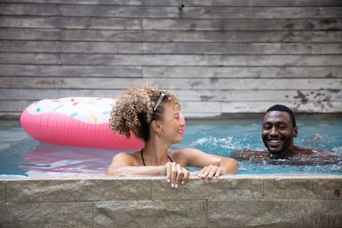 Mixed-race woman and black man enjoying summer pool with pink donut float and smiling