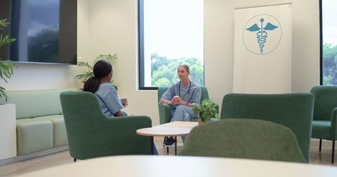 Nurses chatting in clinic lounge holding coffee wearing blue scrubs and stethoscopes