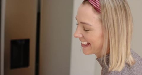 Smiling blonde woman wearing pink headband and gray sweater enjoying cozy kitchen moment