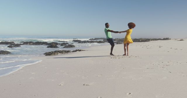 Couple dancing and holding hands on sandy beach during sunrise, conveying a carefree and romantic atmosphere. Perfect for themes related to romance, travel, togetherness, happiness, and beach vacations.