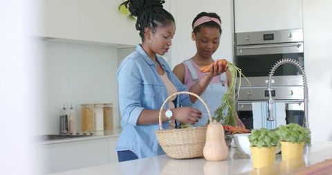 African mother and daughter preparing fresh vegetables on modern kitchen island