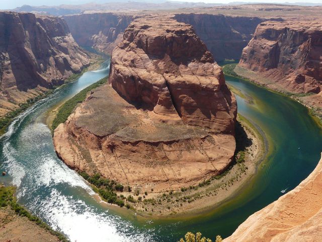 Captivating perspective of Horseshoe Bend in the Grand Canyon with the Colorado River wrapping around the rugged red rock formations. Ideal for travel brochures, adventure blogs, nature documentaries, and educational materials focusing on geography and natural wonders.