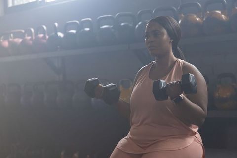 Determined african american woman lifting dumbbells on bench in moody gym light