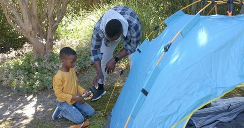 Father son assembling blue dome tent, hammering stake, family bonding