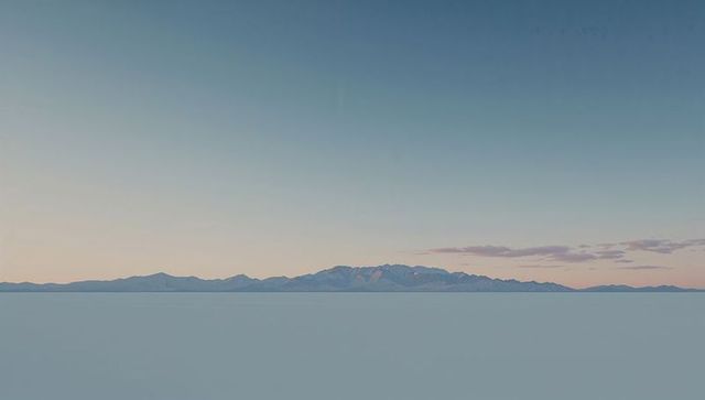 Minimalist salt flat stretching to distant mountain range at pastel sunrise