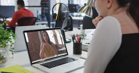 Professional woman watching remote video meeting on laptop in open-plan office
