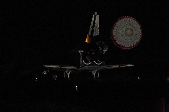 Space Shuttle Endeavour is seen during its final landing on Runway 15 at NASA's Kennedy Space Center on June 1, 2011, captured in dark conditions with its drag chute deployed. This historic event marks the end of Endeavour's 25th mission (STS-134) which delivered the Alpha Magnetic Spectrometer-2 (AMS) and the Express Logistics Carrier-3 (ELC-3) to the International Space Station. This image can be used for topics related to space exploration, NASA missions, historic space events, and spacecraft engineering.
