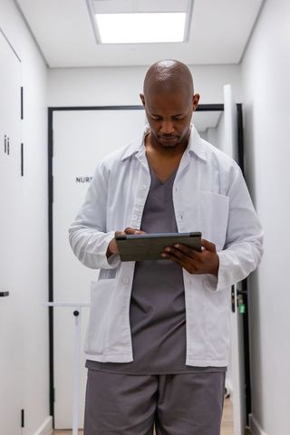 African american male nurse reviewing patient records on tablet in bright clinic corridor