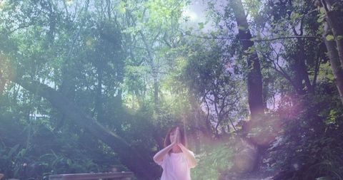 Woman practicing meditation in sunlit forest glade with bench and fallen trunk