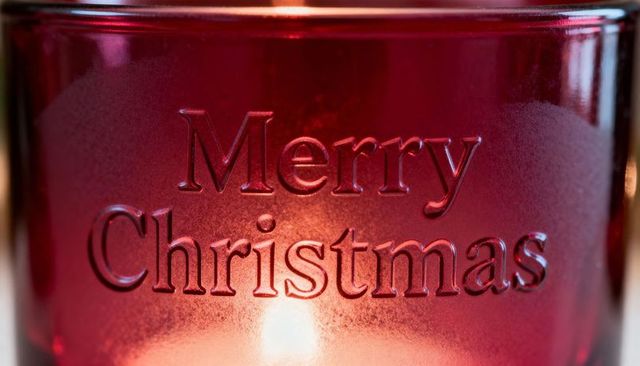 Glowing red frosted candle holder embossed merry christmas with warm candlelight glow