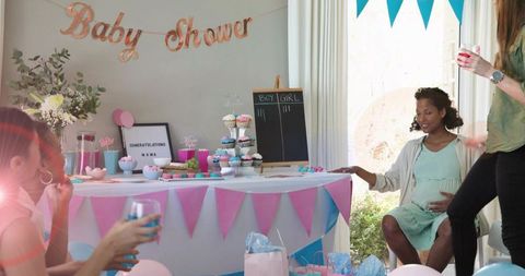 Pregnant woman celebrating baby shower at home with pastel banners, cupcakes, gifts
