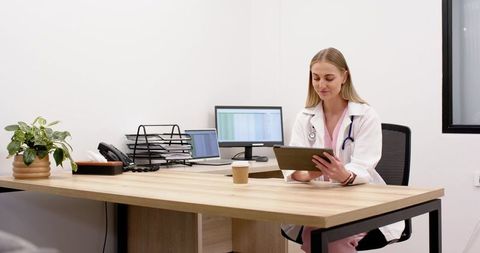 Female clinician reviewing tablet with laptop and stethoscope in modern clinic office