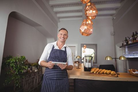 Smiling Baker in Apron Arranging Fresh Baguettes at Modern Bakery