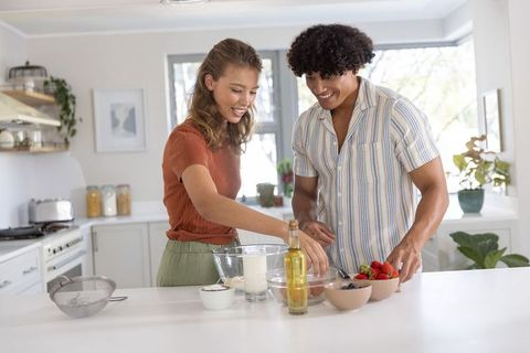 Couple preparing breakfast batter with fresh berries on bright modern kitchen island