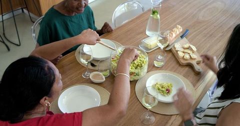 Multigenerational african american women serving pesto pasta salad at home table