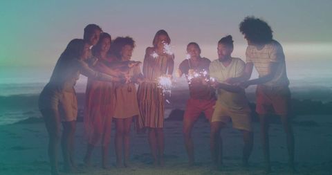Friends celebrating on beach at dusk with sparklers and warm twilight glow