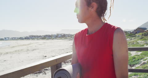 Caucasian Man with Dreadlocks Reflecting at Beach with Yoga Mat