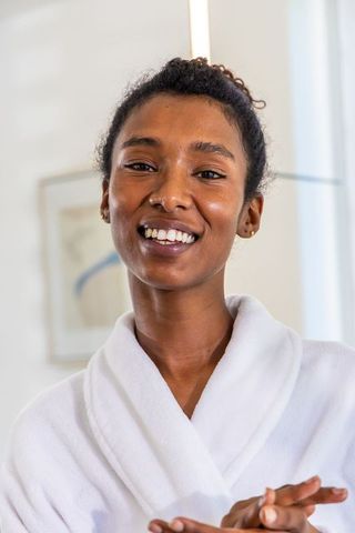 African woman smiling in white bathrobe showing radiant skin and simple stud earrings