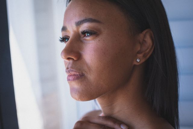 Close up portrait of biracial woman looking out of window in thought. staying at home in isolation during quarantine lockdown.