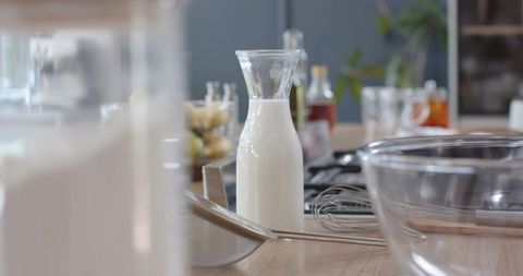 Glass milk carafe with whisk and mixing bowl on rustic wooden countertop for cooking prep