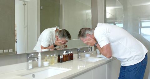 Senior man washing face at minimalist double vanity mirror morning grooming