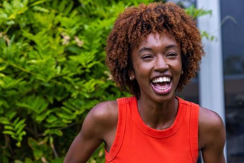 Sunlit african american woman laughing in red tank top leaning forward outdoor portrait