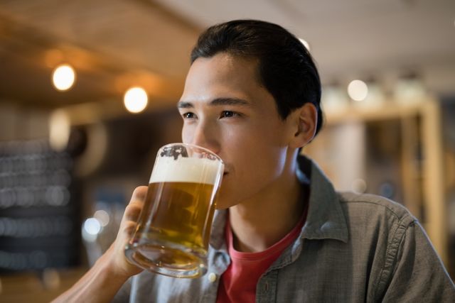 Young man drinking beer in a cozy restaurant, perfect for themes related to leisure, socializing, and relaxation. Ideal for use in advertisements for bars, restaurants, or beer brands, as well as lifestyle blogs and social media posts about casual dining and enjoying beverages.