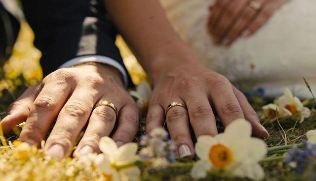 Gold wedding bands resting on mossy meadow with wildflowers, closeup of newlywed hands