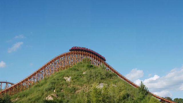 Roller coaster ascending grassy hill on bright day
