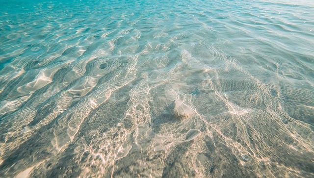 Crystal clear shallow sea with rippled sand, pebbles and shimmering sunlight caustics