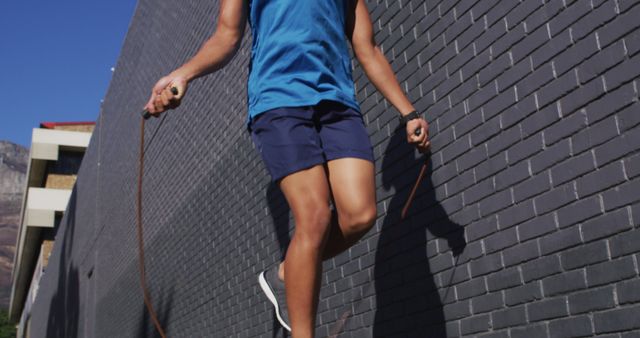 Fit african american man exercising in city, using earphones, skipping with skipping rope in street. fitness and active urban outdoor lifestyle.