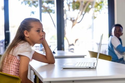 Preteen girl using laptop while african american boy watching in modern sunlit classroom