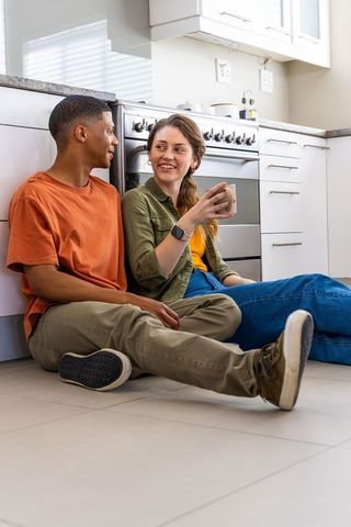Cozy multiracial couple sitting on kitchen floor sharing coffee and conversation