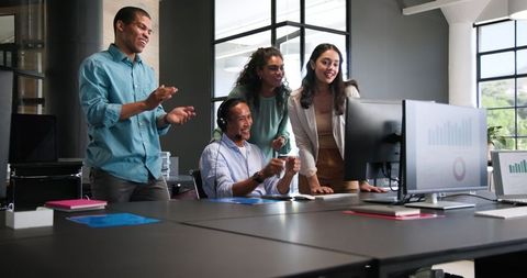 Diverse Team Celebrating Success Around Office Computer