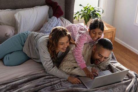 Family watching laptop together in cozy bedroom, morning bonding and relaxation