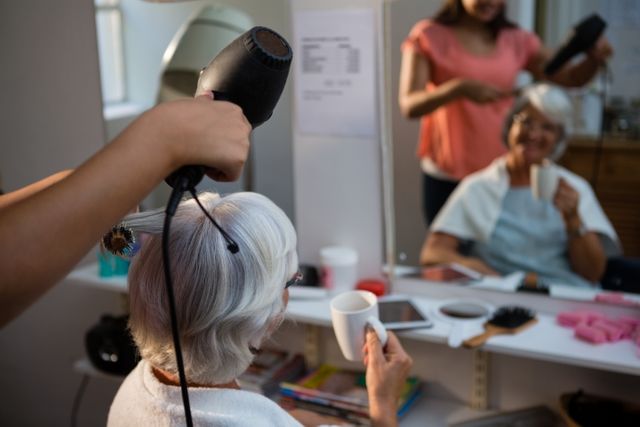 Beautician drying senior woman hair reflecting on mirror in salon