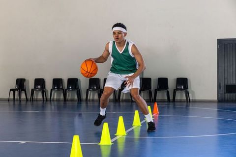 African american basketball player dribbling through cones on indoor court performing agility drill