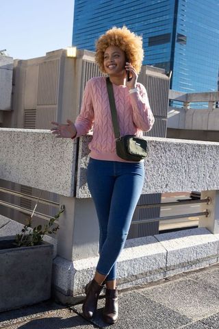 African american woman talking on smartphone while leaning on rooftop parapet, cityscape