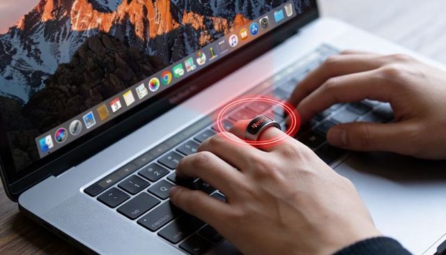 Typing on laptop wearing smart ring with red holographic interface over keyboard