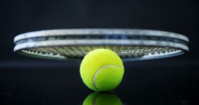 Vivid close-up of a green tennis ball perfectly balanced on a tennis racket against a black background. Ideal for sports advertisements, tennis equipment promotions, coaching and training materials, and general sporting themed content.