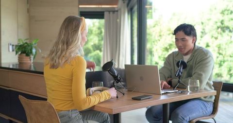Remote podcast duo recording with laptop and professional microphones in bright home studio