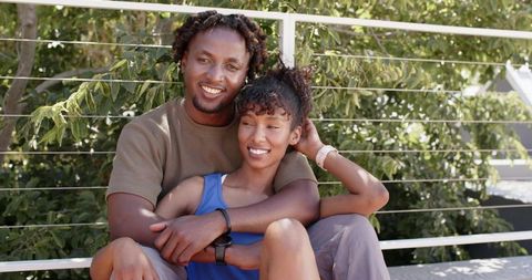 Smiling couple embracing on sunny balcony bench enjoying outdoor moment