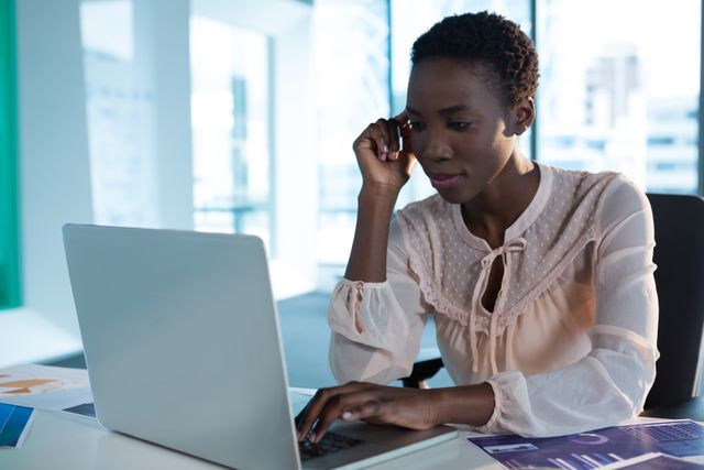 Female executive concentrating on laptop in a modern office environment. Ideal for use in business, technology, and corporate productivity contexts. Suitable for illustrating professional work settings, business technology usage, and modern office environments.