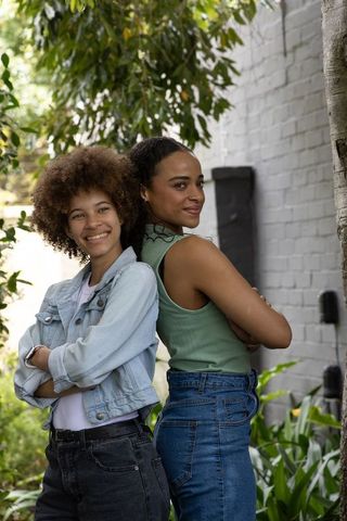 Confident african women standing back-to-back in sunlit courtyard wearing denim and green
